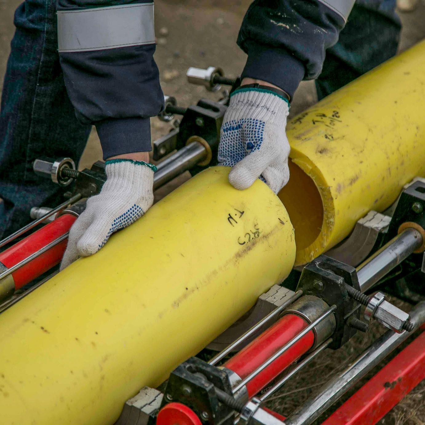 Close-up view of a worker using equipment to install yellow pipes outdoors, focusing on hands and tools.