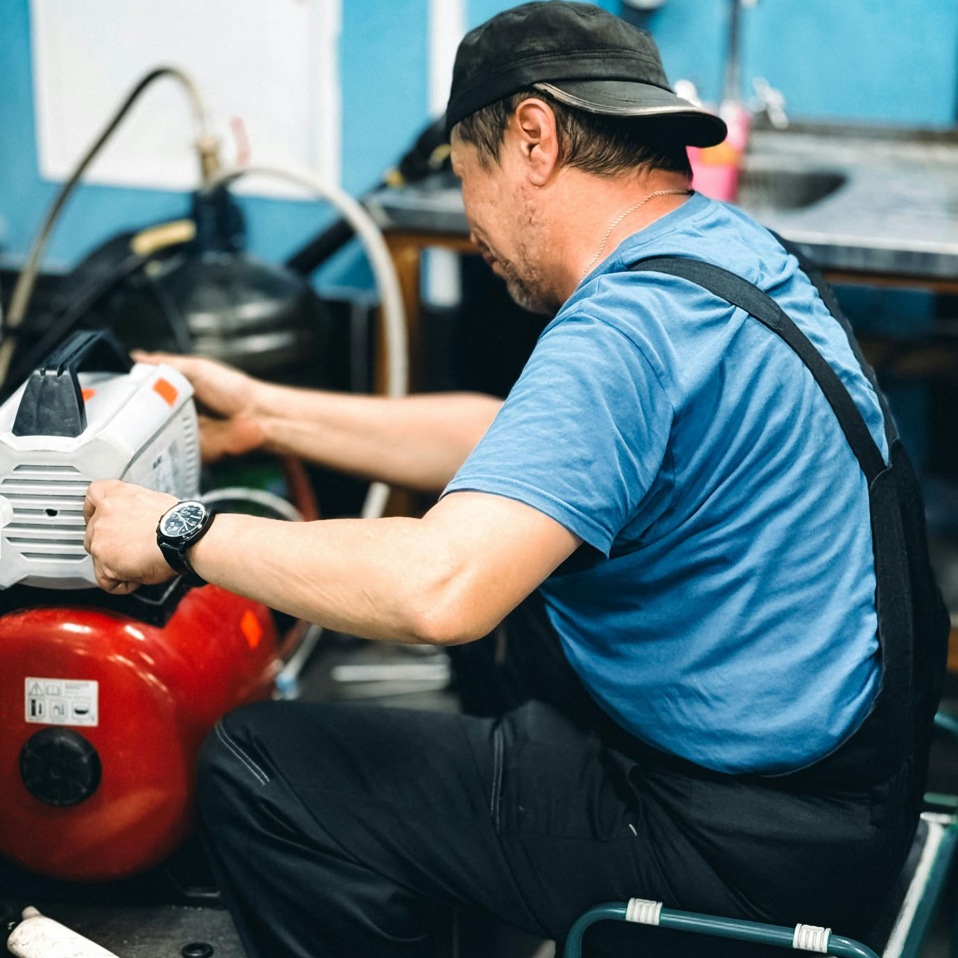 Repairman in blue overalls working diligently on machinery in an industrial workshop.