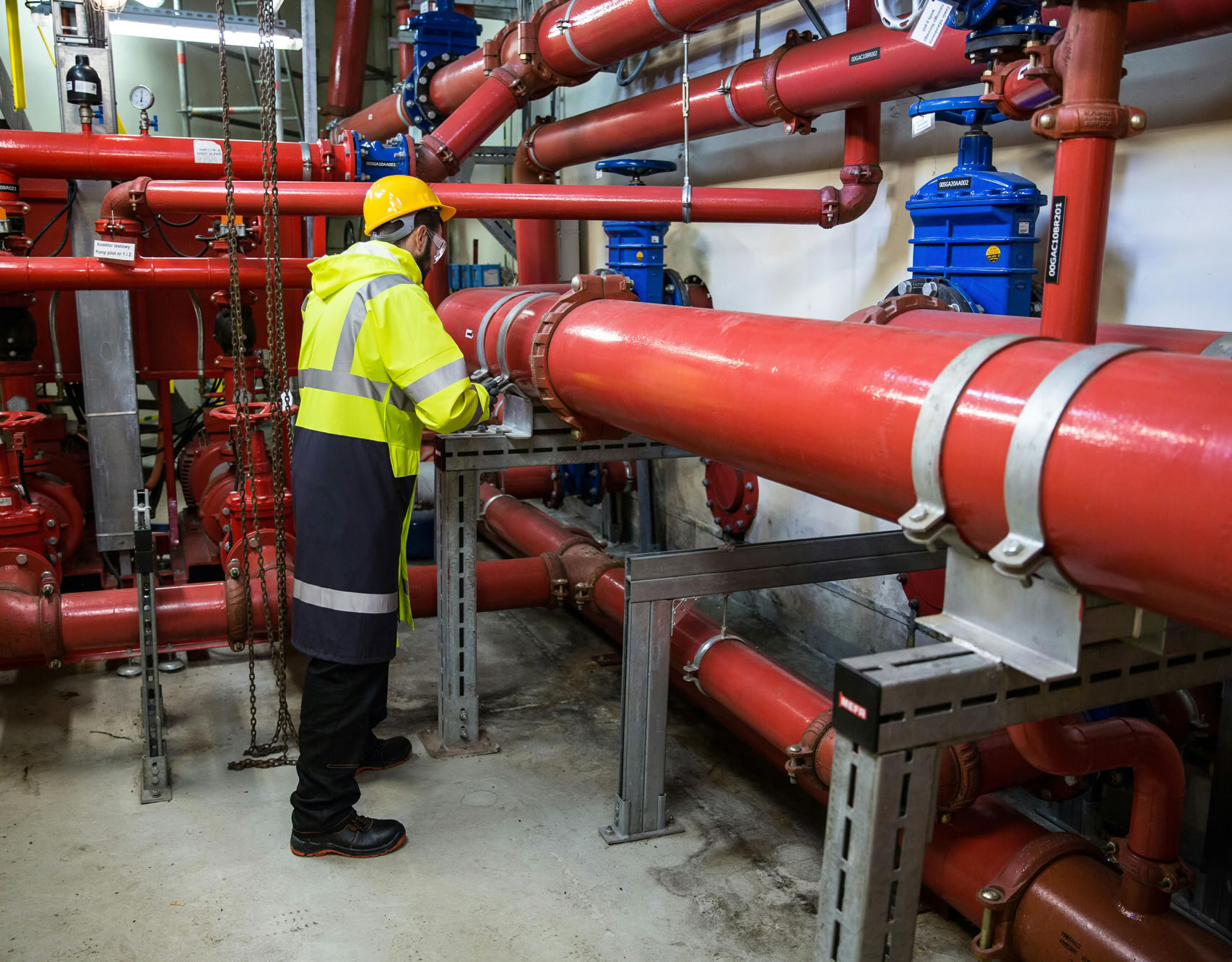 Engineer with safety gear inspecting red industrial piping system indoors.