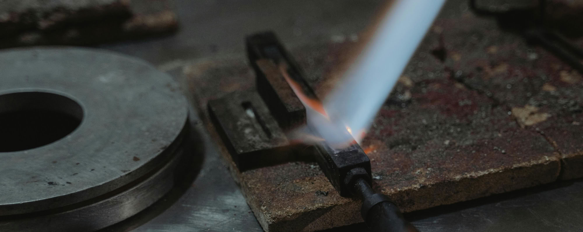 Close-up of a lit blowtorch in an industrial workshop setting.